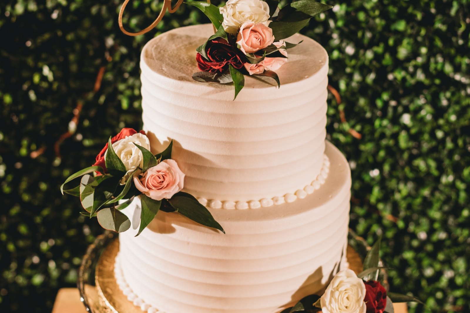 A two-tier wedding cake with horizontal buttercream ridges and fresh pink, red, and white roses by Sweet Escape Cake Company in Indianapolis.