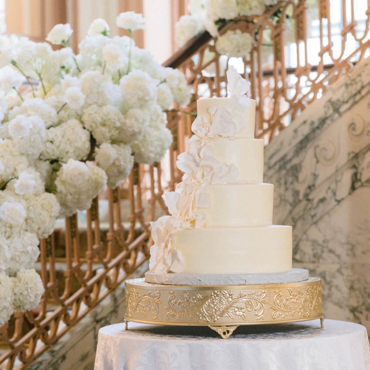 A four-tier cream wedding cake on a gold stand that feeds about 130 guests, by Sweet Escape Cake Company in Indianapolis.