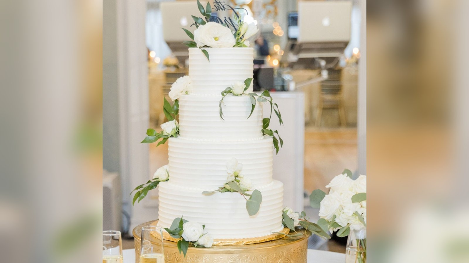 A four-tier white buttercream wedding cake on a gold stand at an Indianapolis reception, by Sweet Escape Cake Company.