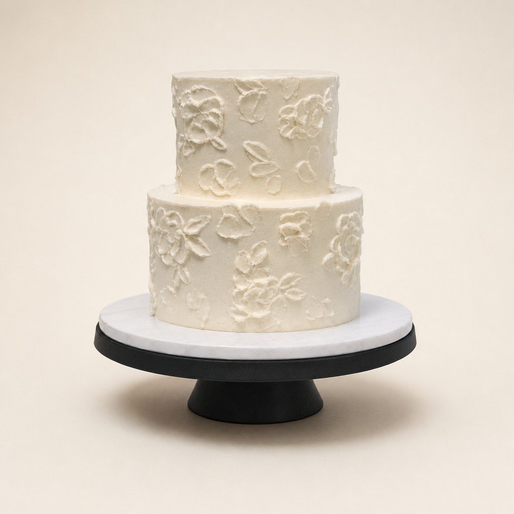 A two-tier wedding cake with piped floral detail on a cake stand, about 36 wedding servings, by Sweet Escape Cake Company.