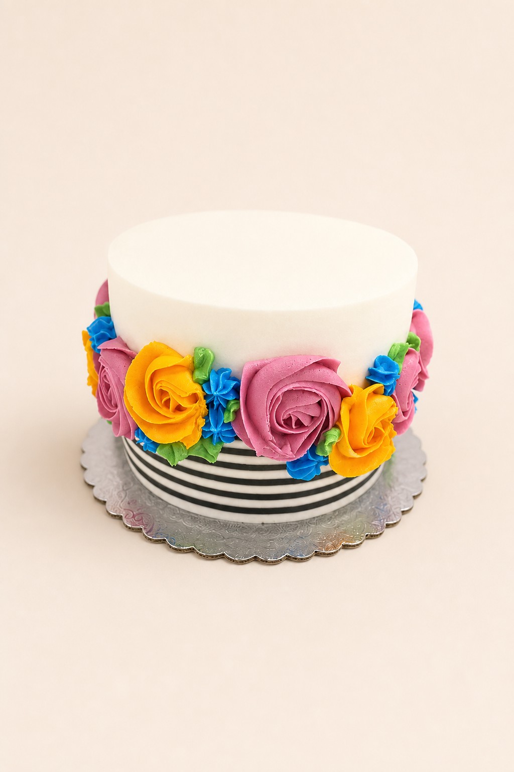 A single-tier round white buttercream cake featuring vibrant piped floral decorations and a bold black and white striped base.