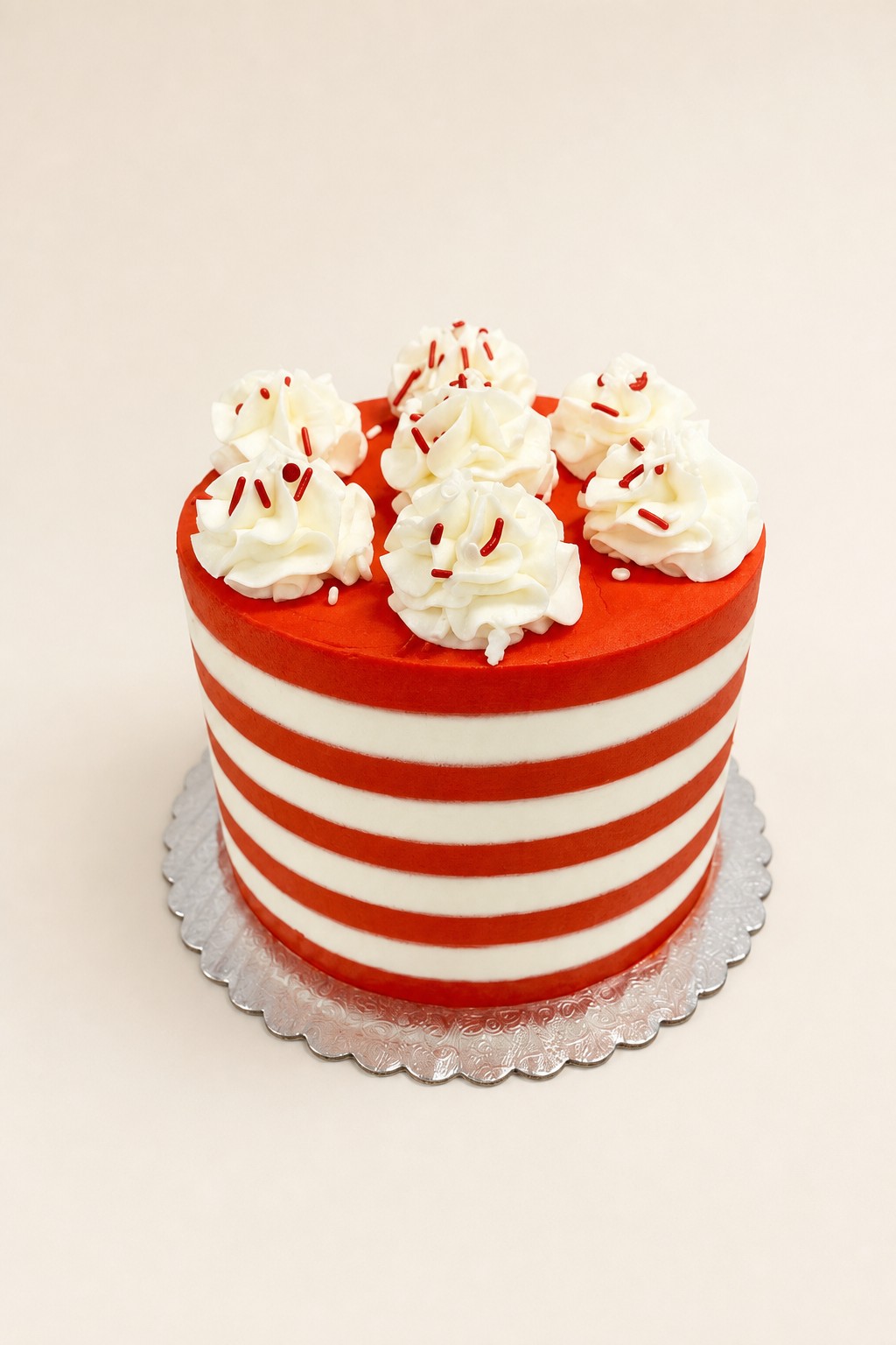 A festive round single-tier cake decorated with alternating horizontal red and white buttercream stripes and topped with white piped rosette