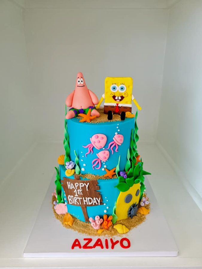 A vibrant two-tiered SpongeBob SquarePants themed 1st birthday cake, featuring fondant figurines of SpongeBob and Patrick, an edible underwa