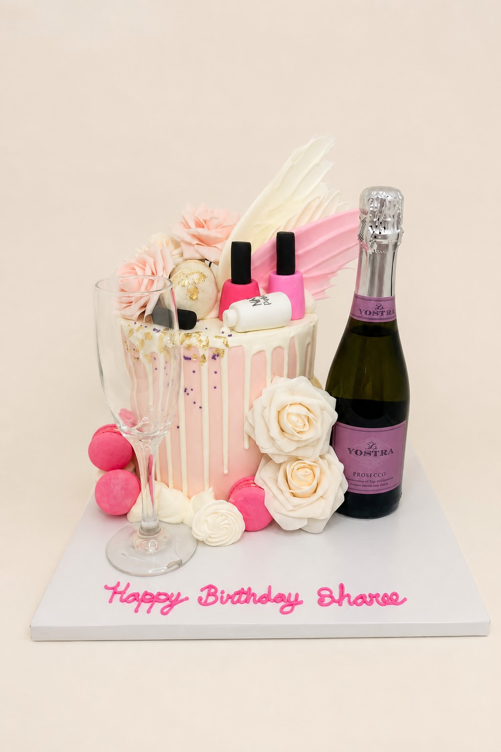 A elegant pink and white drip birthday cake decorated with pink macarons, various sugar flowers, gold leaf, purple sprinkles, and fondant na