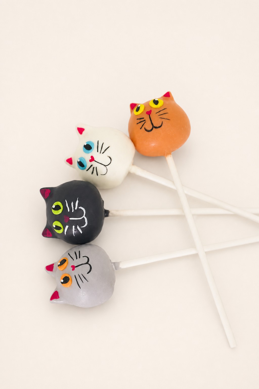 A charming collection of cat-themed cake pops in white, black, grey, and orange, each individually decorated with unique facial expressions 