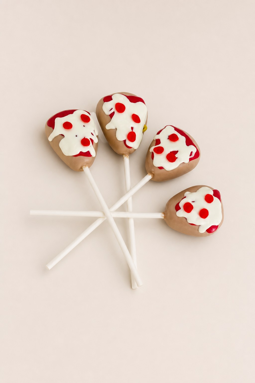 Four pizza-themed cake pops on sticks, decorated with white icing, red pepperoni dots, red drizzle, and yellow sprinkles on a white platter.