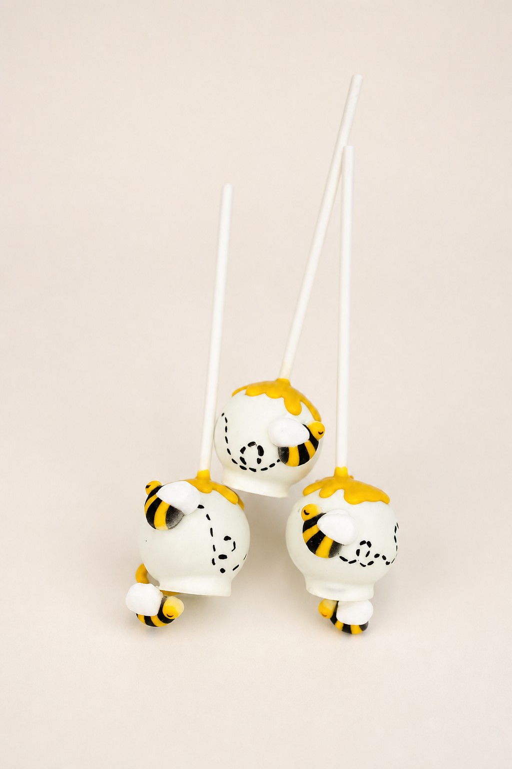 White bee-themed cake pops decorated with yellow drip, black sprinkles, and adorable bumblebee fondant figures.