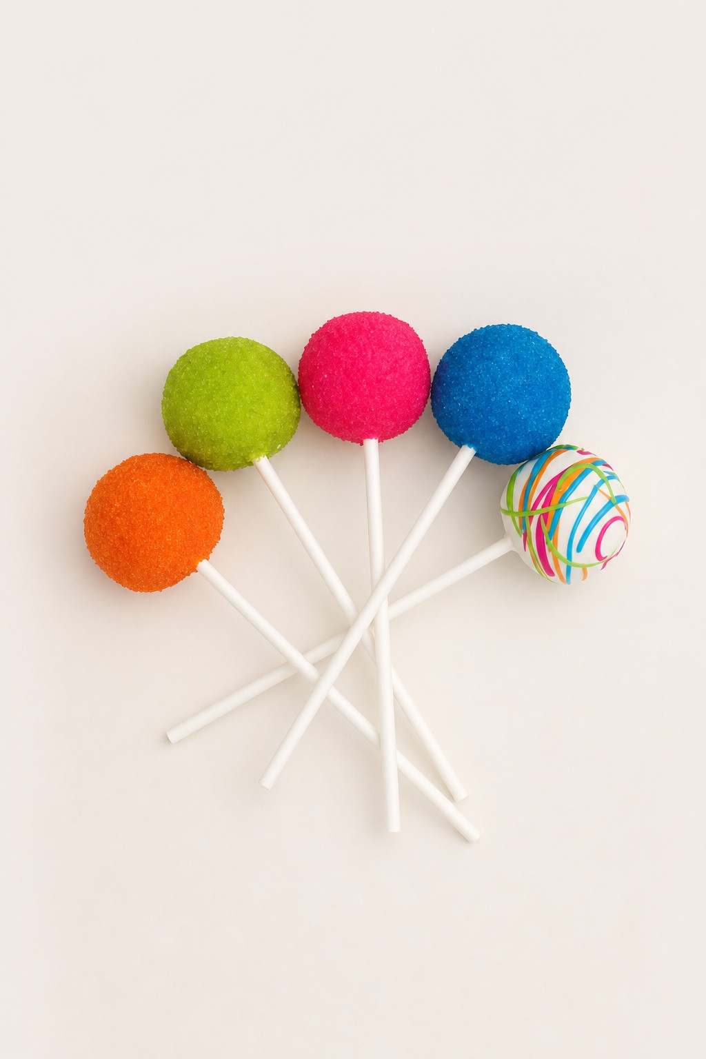 Colorful round cake pops, some coated in vibrant sugar sprinkles (orange, green, pink, blue) and one white cake pop decorated with multicolo