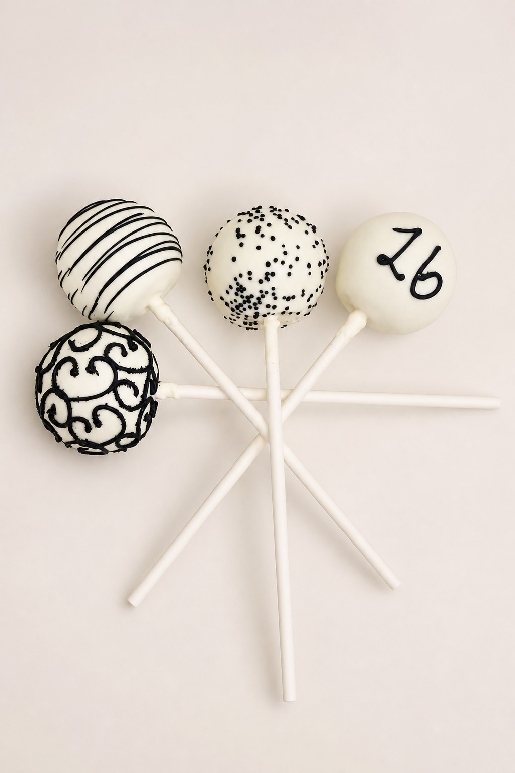 Elegant black and white cake pops with various designs including stripes, polka dots, intricate swirls, and a hand-drawn '26' numeral, finis