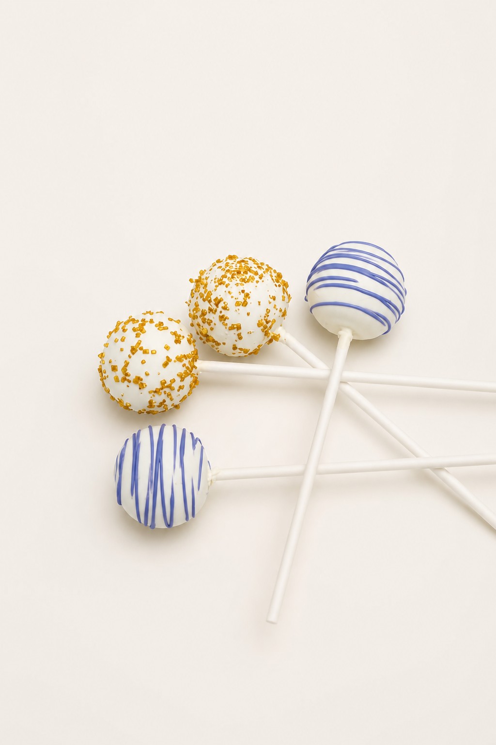 White cake pops decorated with gold sprinkles and blue or purple drizzle, presented on a white rectangular platter.