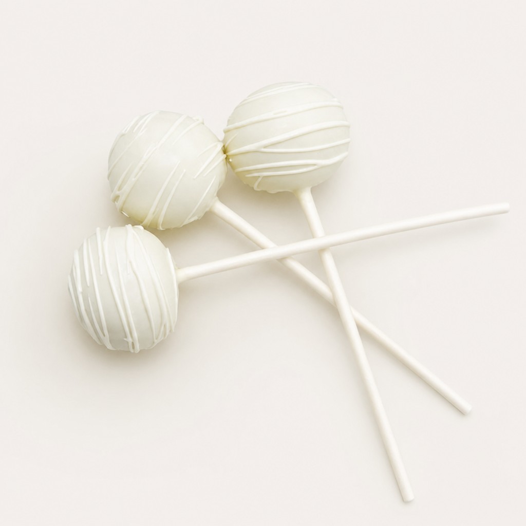 Three elegant white cake pops with delicate white drizzle presented on a white plate.