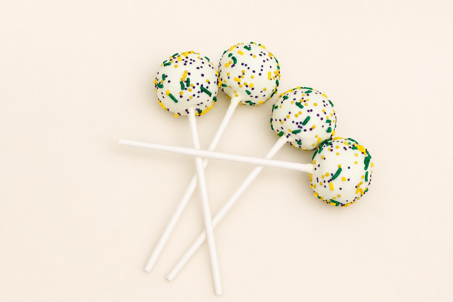 White cake pops on sticks, decorated with green, purple, and gold sprinkles, perfect for a Mardi Gras celebration.