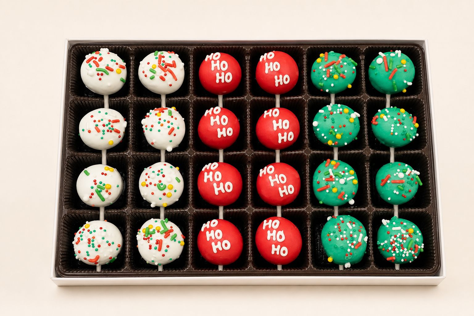 A festive assortment of Christmas-themed cake pops, including red ones with 'HO HO HO' in white royal icing, and white and green ones covere