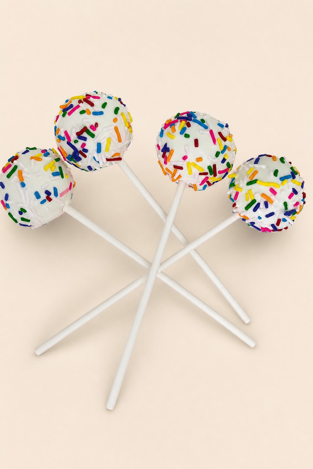 White cake pops coated in colorful rainbow sprinkles, presented on white sticks.