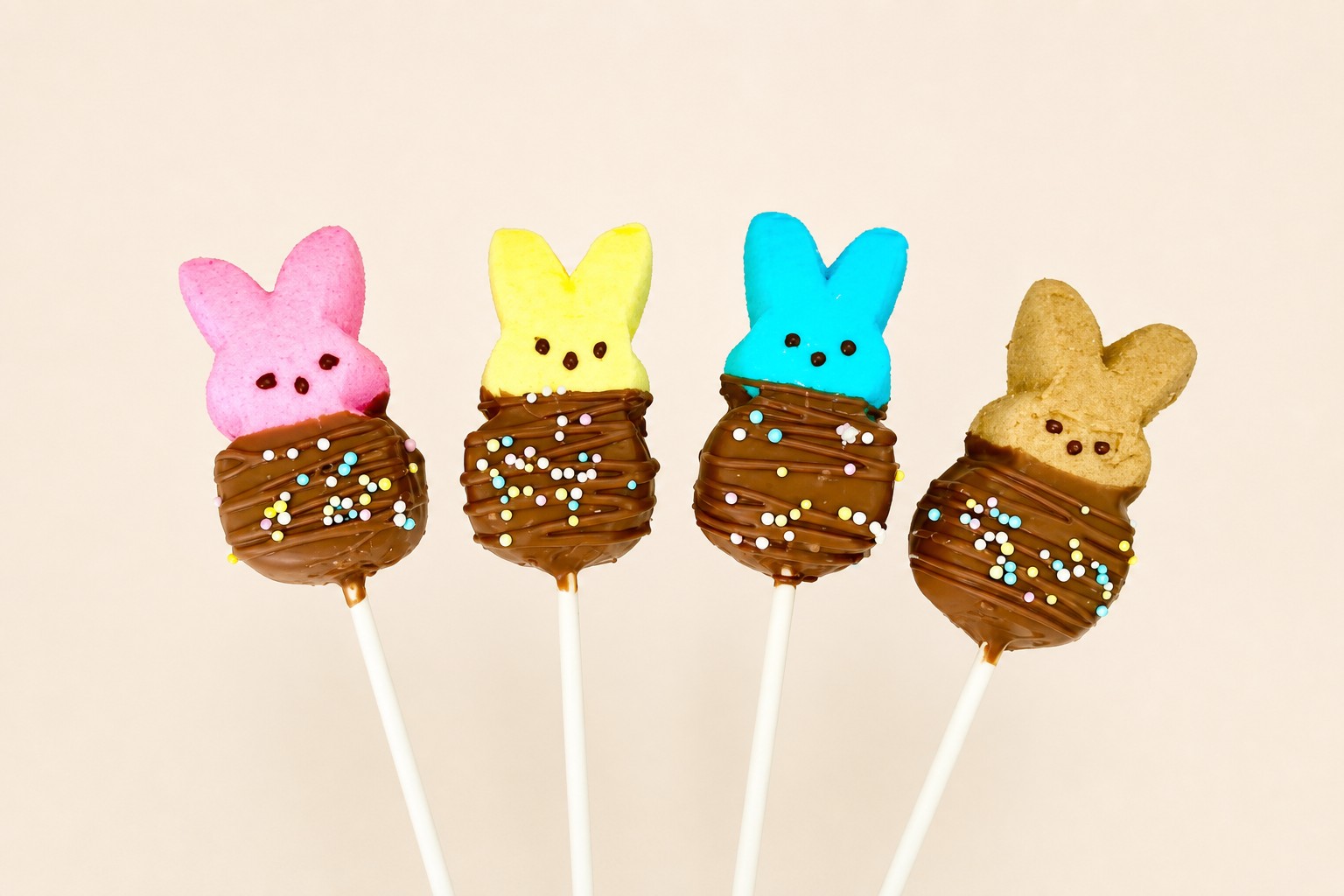 A set of colorful marshmallow Peeps, including pink, yellow, blue, and brown, dipped in chocolate with pastel sprinkles, served on sticks, p