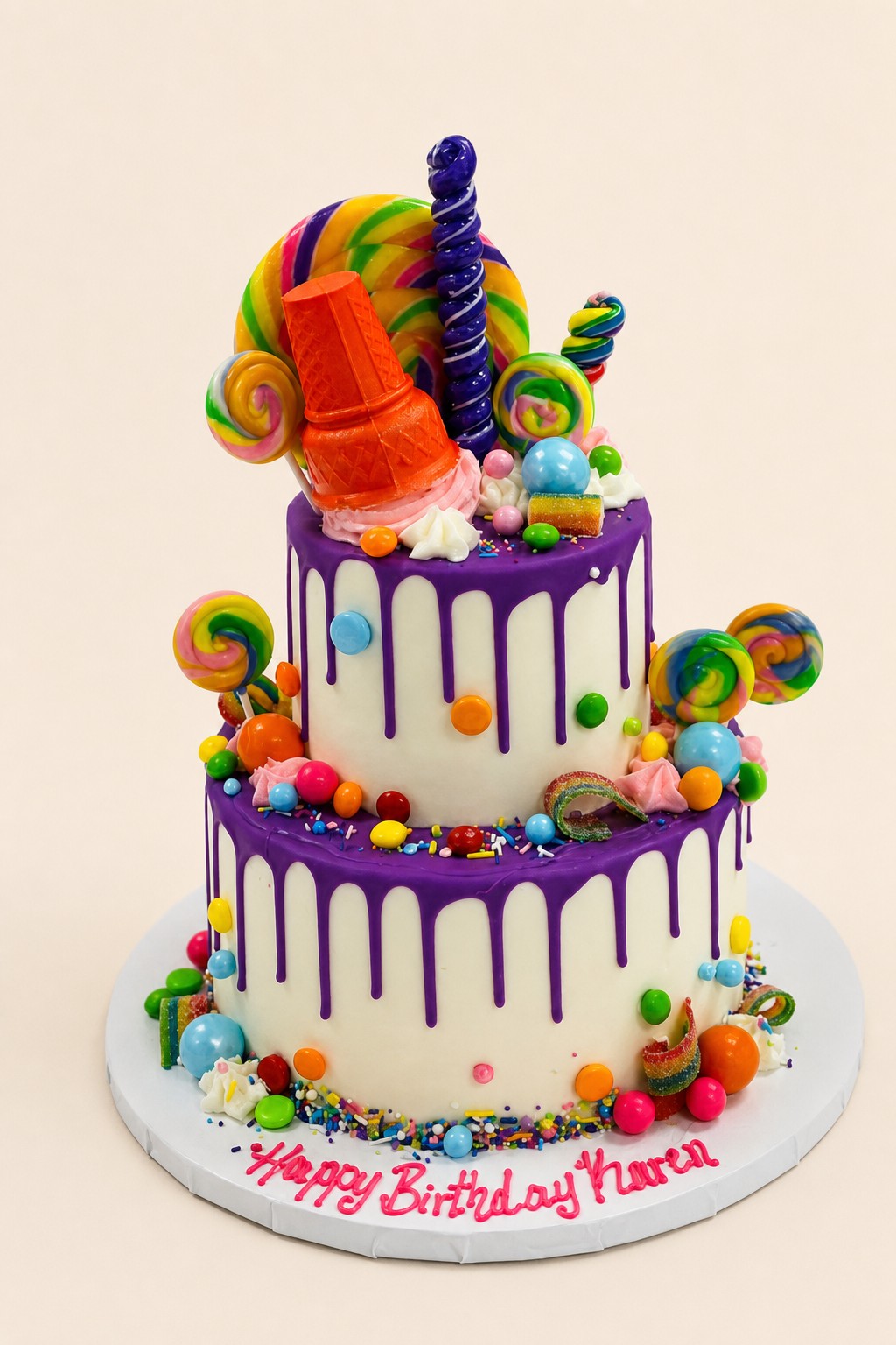 A two-tiered white birthday cake with purple drip icing, generously decorated with an assortment of colorful candies, lollipops, and sprinkl