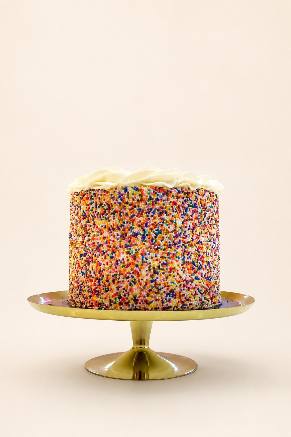 A single-tier round birthday cake fully covered in vibrant rainbow sprinkles with a decorative swirl of white buttercream frosting on top, p