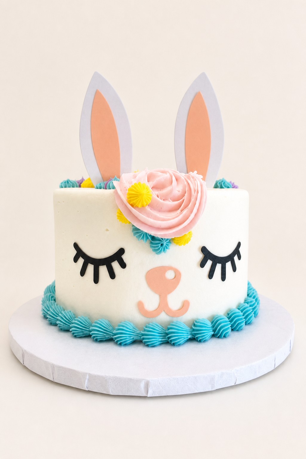 A charming bunny-themed single-tier birthday cake featuring white buttercream, pink and yellow frosting swirls, blue piped border, black pip