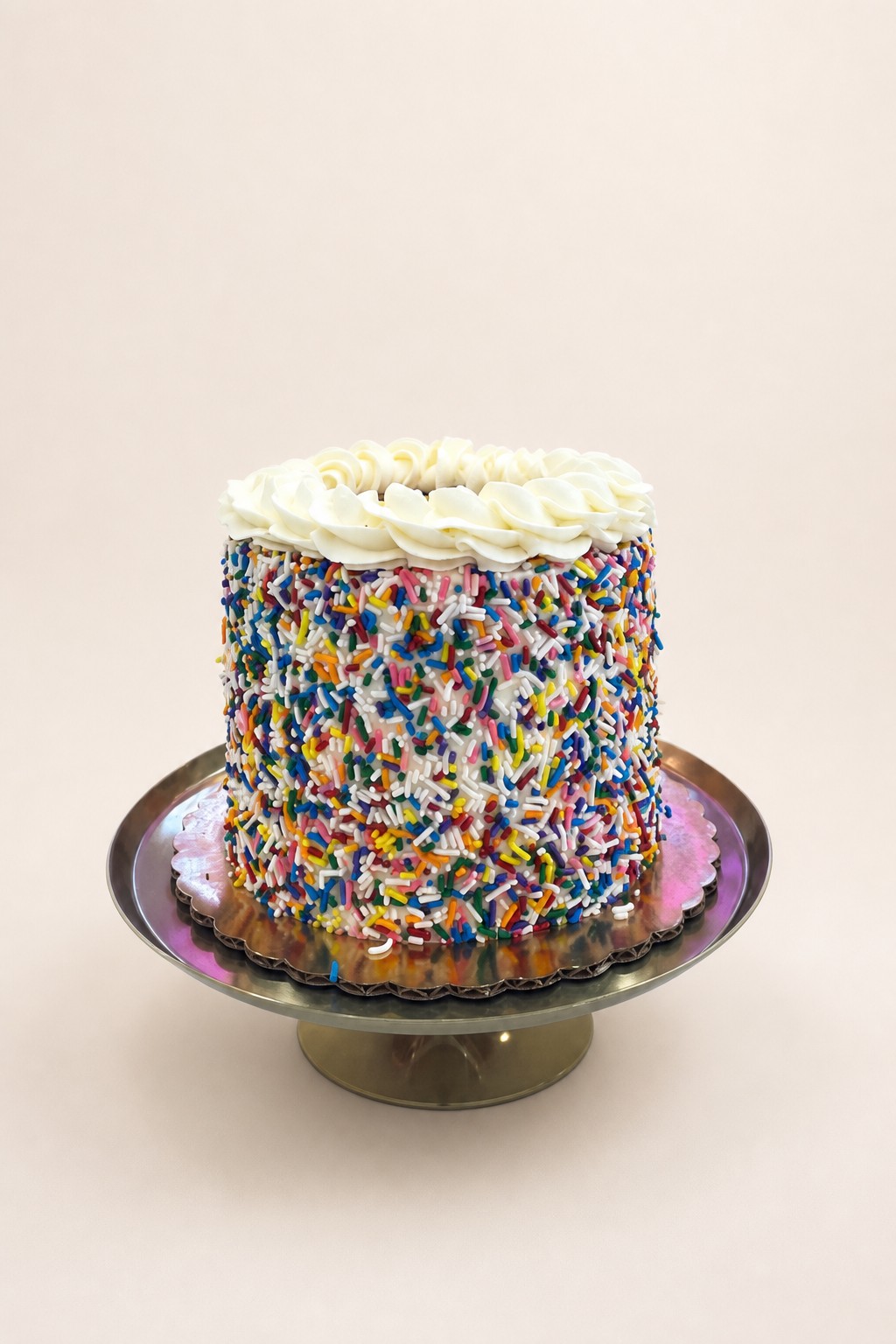 A round birthday cake covered in vibrant multi-colored sprinkles with white buttercream frosting swirls on top.