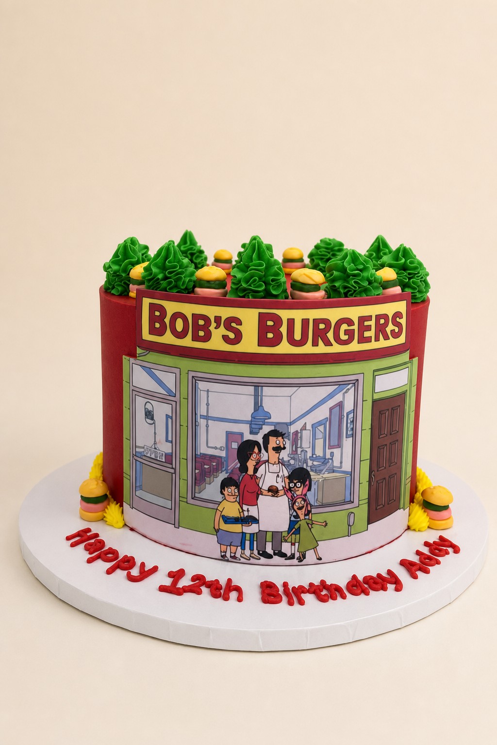 A vibrant red Bob's Burgers themed birthday cake featuring an edible image of the restaurant and characters, topped with green frosting tree