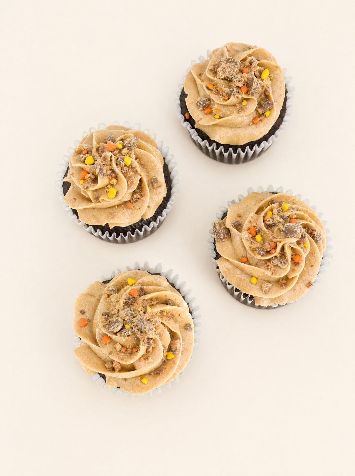 Delicious chocolate cupcakes topped with swirled tan or peanut butter-colored buttercream frosting and crunchy candy crumbles, scattered on 