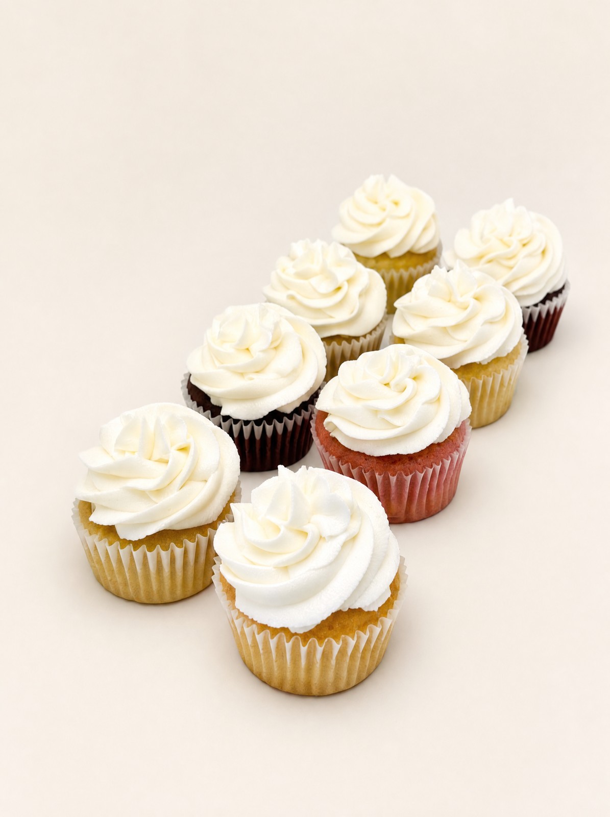 Assorted cupcakes with white buttercream frosting and colorful wrappers, displayed on a white plate surrounded by scattered colorful sprinkl