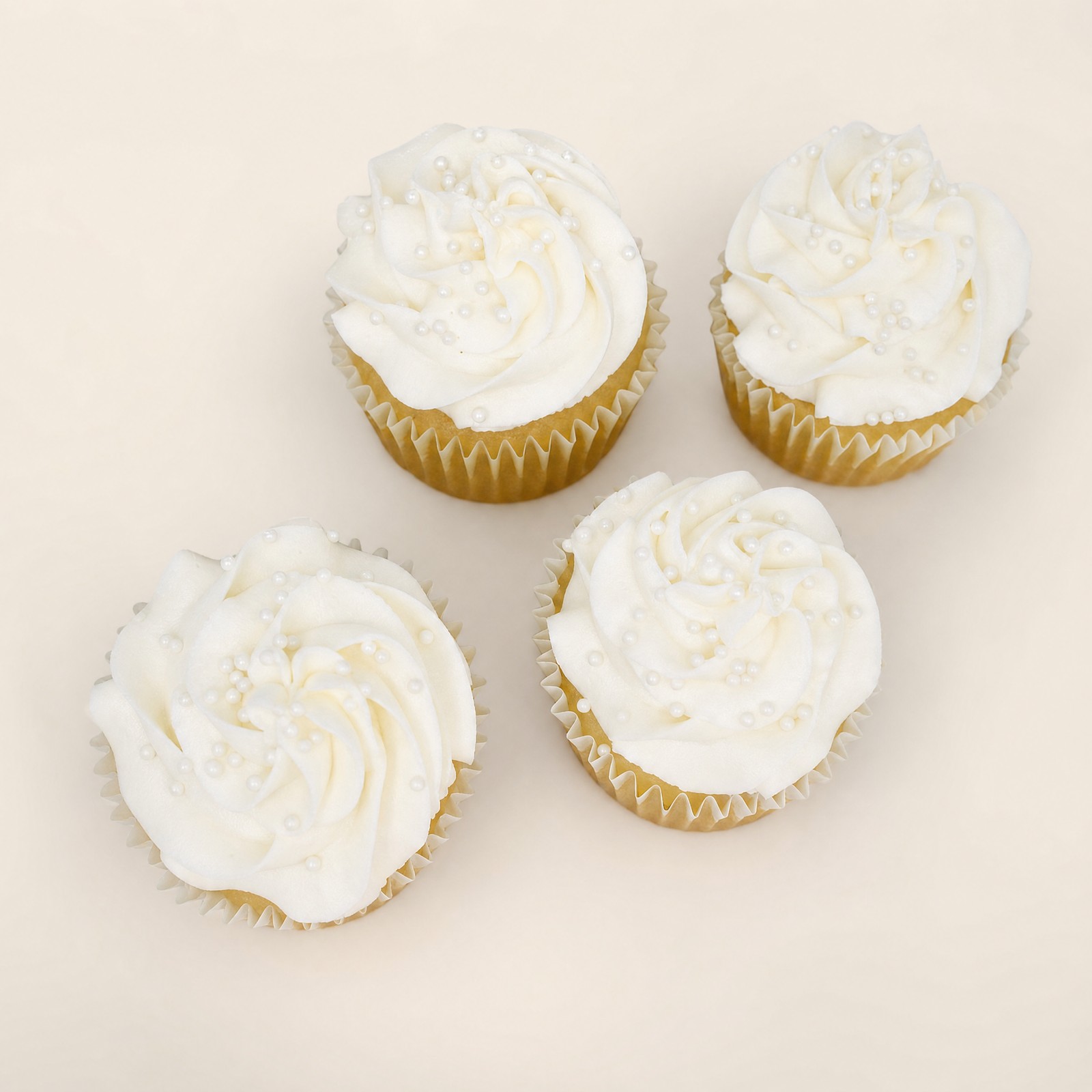 Elegant white cupcakes topped with swirled white buttercream frosting and small white pearl sprinkles, perfect for a wedding or special occa