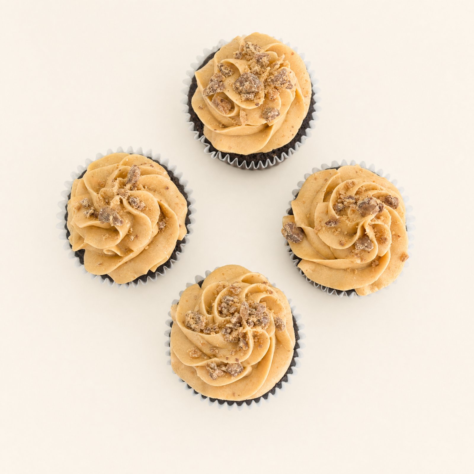 Four chocolate cupcakes topped with a swirl of light brown peanut butter flavored buttercream and a generous sprinkle of crushed candy piece