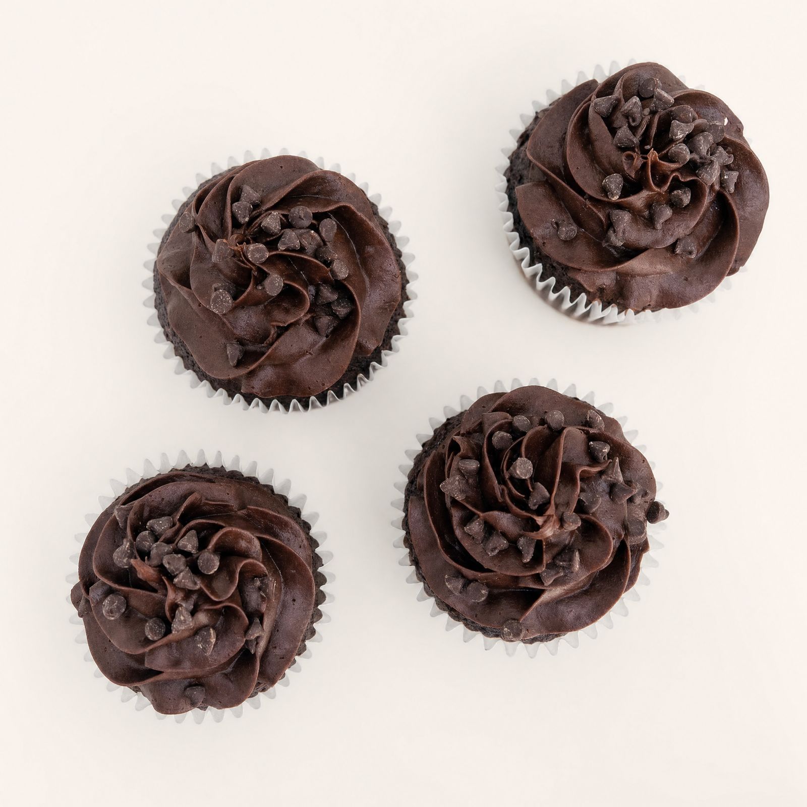 Four decadent chocolate cupcakes topped with rich, swirled chocolate buttercream frosting and mini chocolate chips, presented on a clean whi