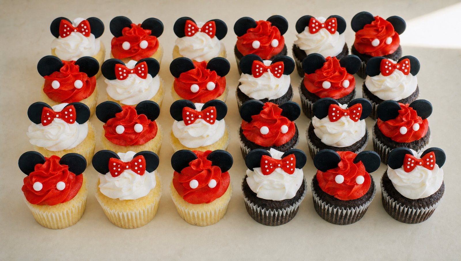 An assortment of Mickey and Minnie Mouse themed cupcakes featuring red and white buttercream frosting, black fondant ears, and red polka dot
