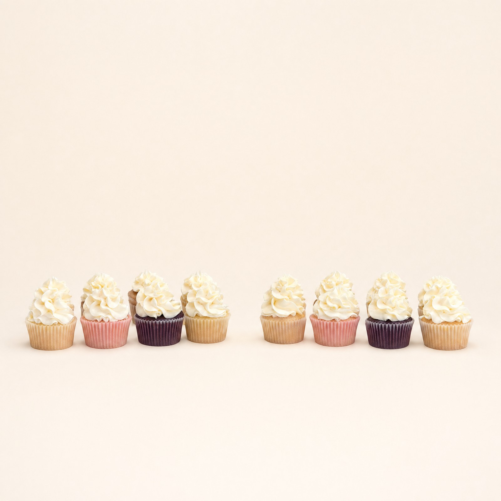 Two clear plastic containers hold a total of twelve cupcakes featuring swirled white frosting and wrappers in light pink, tan, and dark purp