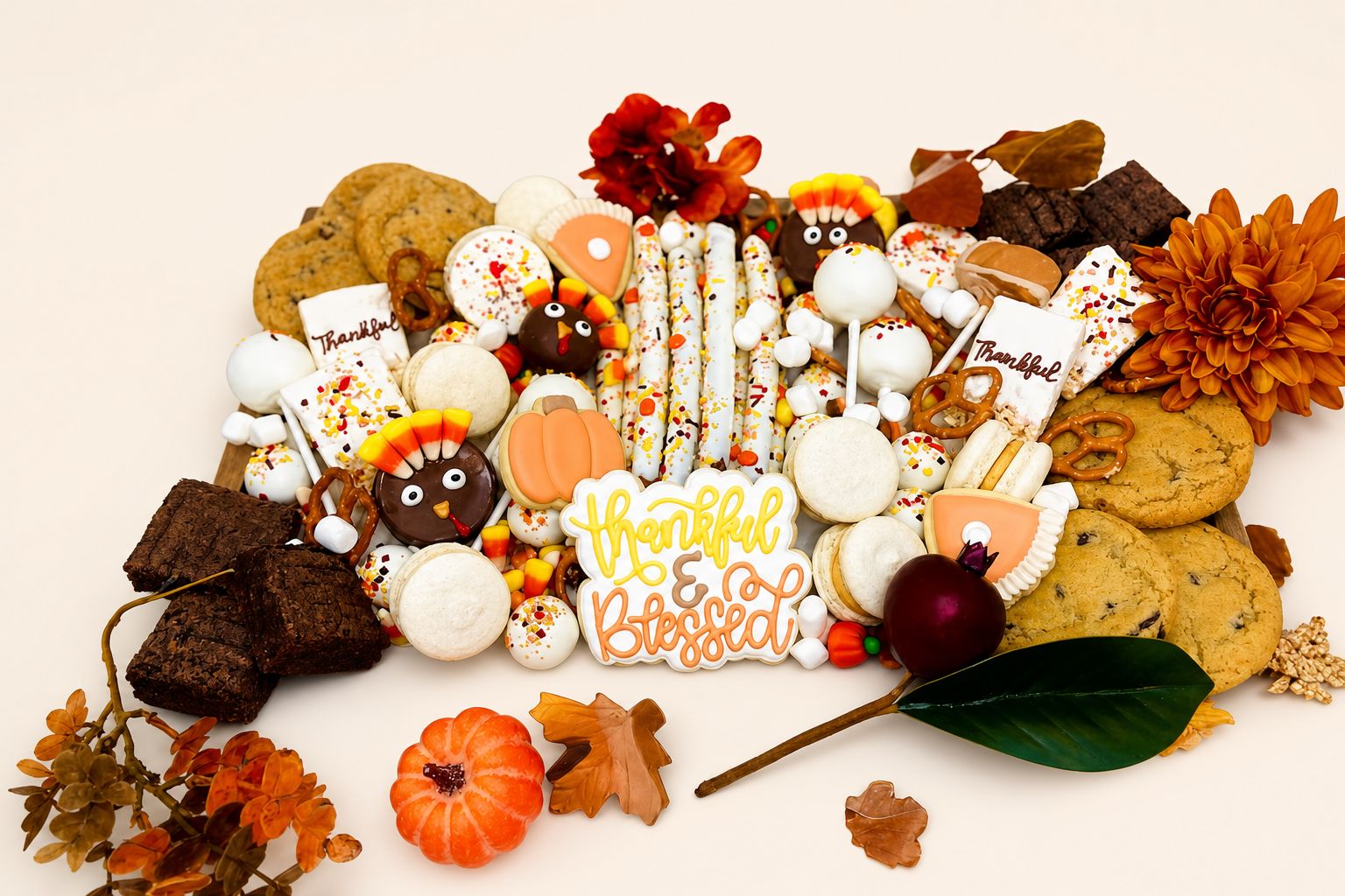 A festive Thanksgiving dessert bar featuring an assortment of fall-themed decorated cookies, turkey cake pops, pumpkin pie cookies, macarons