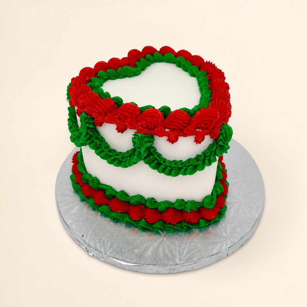 A heart-shaped white cake decorated with festive red and green buttercream ruffles and swirls, ideal for a holiday celebration.
