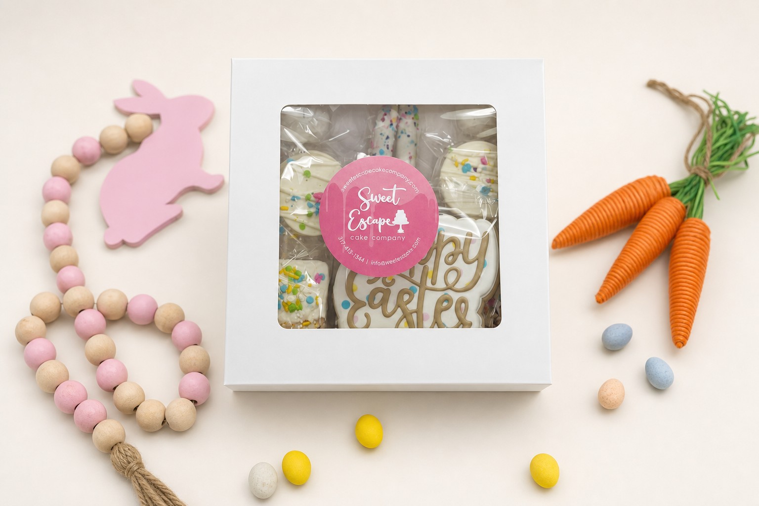 A white window box filled with assorted Easter-themed treats, including royal icing decorated cookies and sprinkle-covered desserts from Swe