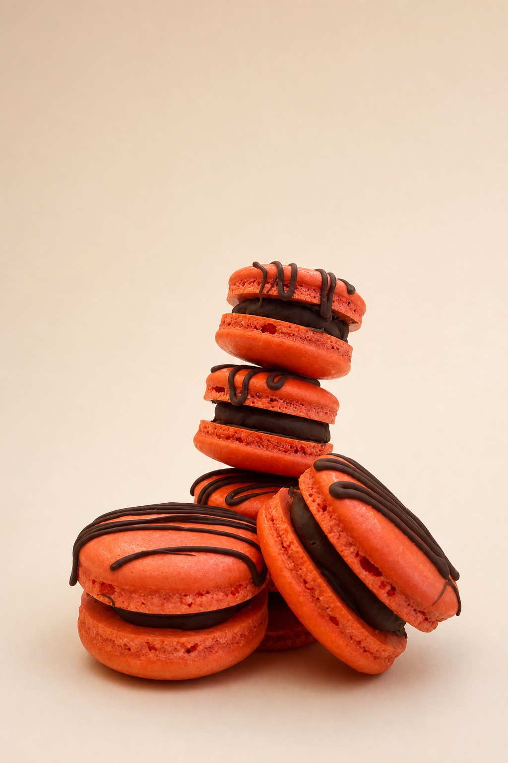 A stack of vibrant orange macarons filled with dark chocolate ganache and drizzled with dark chocolate on a golden tray.